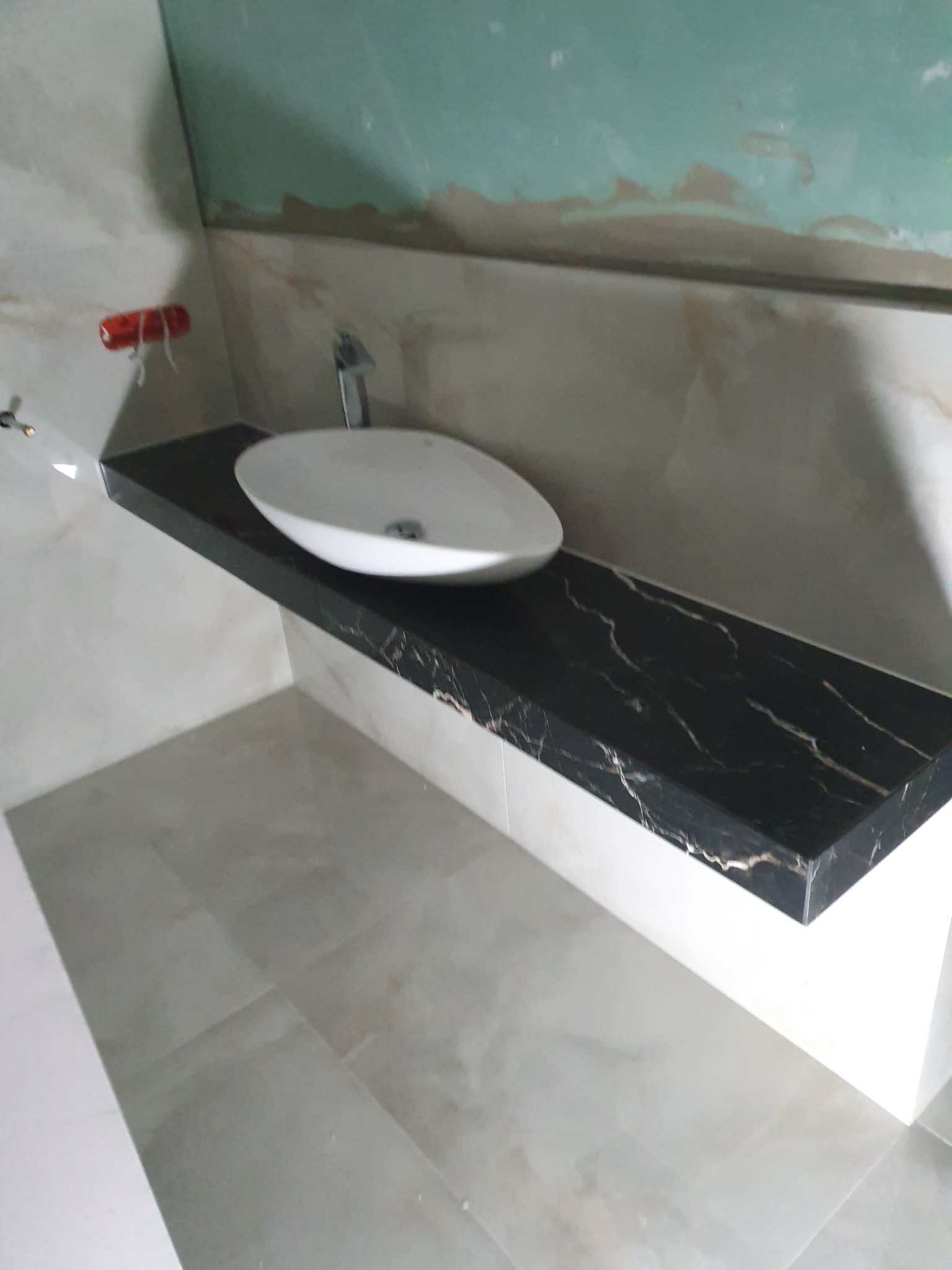 Biała umywalka nablatowa na czarnym blacie z marmurowym wzorem, zamontowana w łazience z szarymi płytkami podłogowymi i częściowo wykończonymi ścianami.