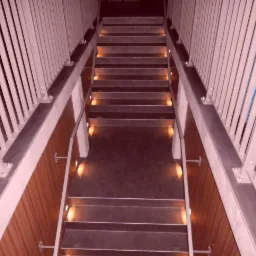 Schody z podświetleniem LED wbudowanym w stopnie, widok z góry, nowoczesne balustrady z pionowych prętów.