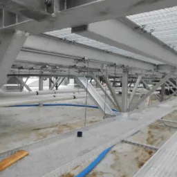 Metalowa konstrukcja wsporcza pod sufitem z widocznymi rurami i korytkami kablowymi, w trakcie instalacji.
