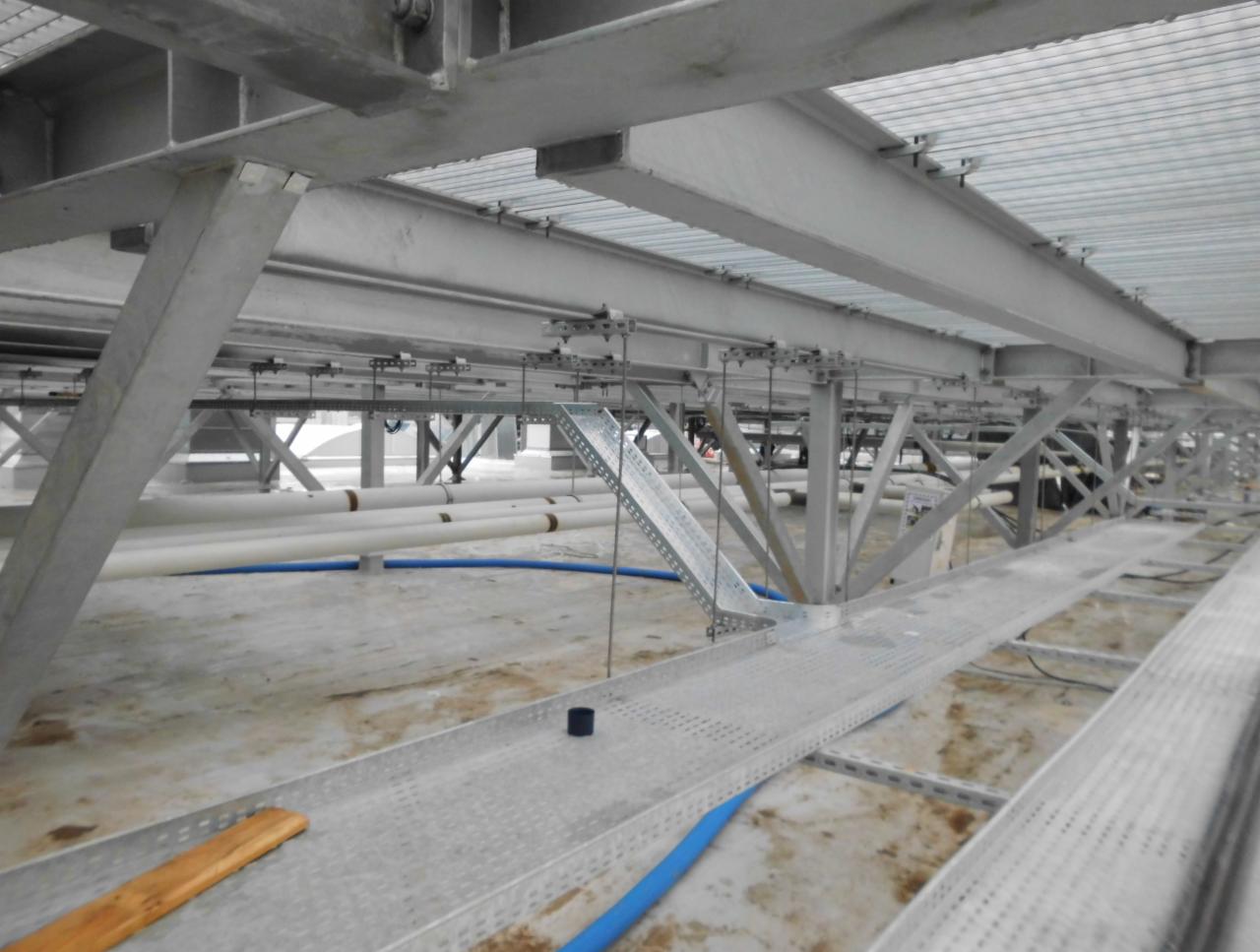 Metalowa konstrukcja wsporcza pod sufitem z widocznymi rurami i korytkami kablowymi, w trakcie instalacji.