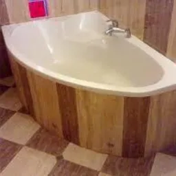 Narożna wanna z obudową z jasnego drewna o pionowym układzie desek, chromowana bateria, płytki podłogowe w szachownicę, fragment ściany wyłożonej płytkami w odcieniach beżu.