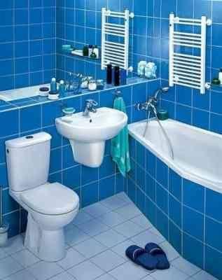 Niebieska łazienka z białą armaturą: umywalka, toaleta, wanna i grzejniki drabinkowe. Na podłodze leżą niebieskie klapki.