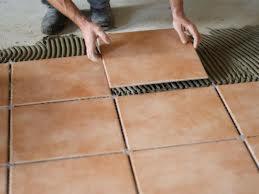 Układanie brązowych płytek podłogowych na zaprawie, widoczne ręce glazurnika i część ułożonej powierzchni.