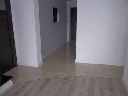 Błyszcząca, świeżo wycyklinowana podłoga schodów z jasnego drewna przechodząca w korytarz z podłogą w odcieniach beżu, widok z dołu schodów.