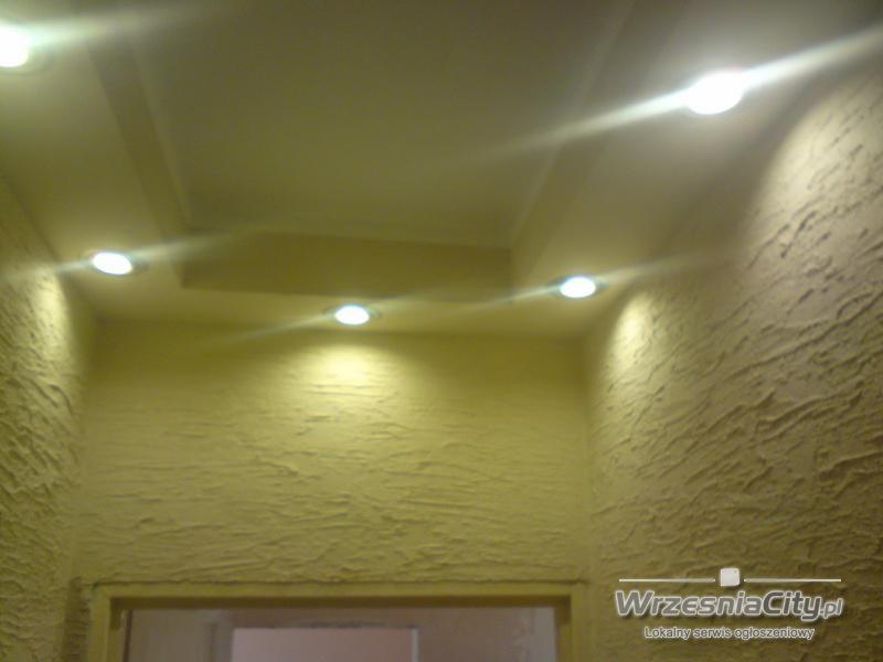 Żółta ściana z fakturą i zamontowane oświetlenie punktowe w suficie podwieszanym z elementami dekoracyjnymi.