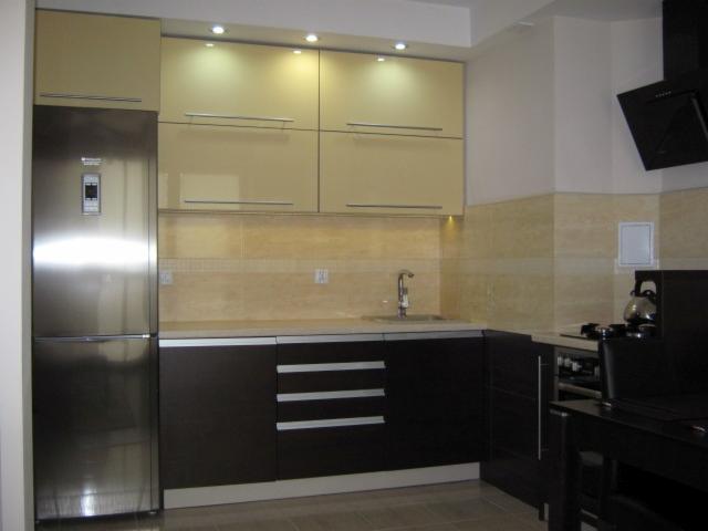 Nowoczesna kuchnia z beżowymi szafkami górnymi z podświetleniem LED i ciemnobrązowymi szafkami dolnymi, stalowa lodówka side-by-side, kamienny backsplash i czarny okap nad płytą gazową z czajnikiem.