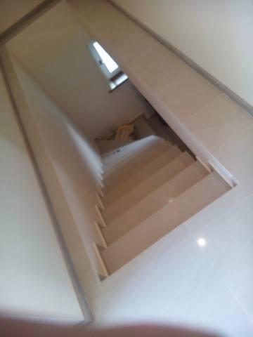 Wykończone schody wewnątrz domu, pokryte jasnymi płytkami, widok z góry w kierunku okna na końcu biegu schodów.