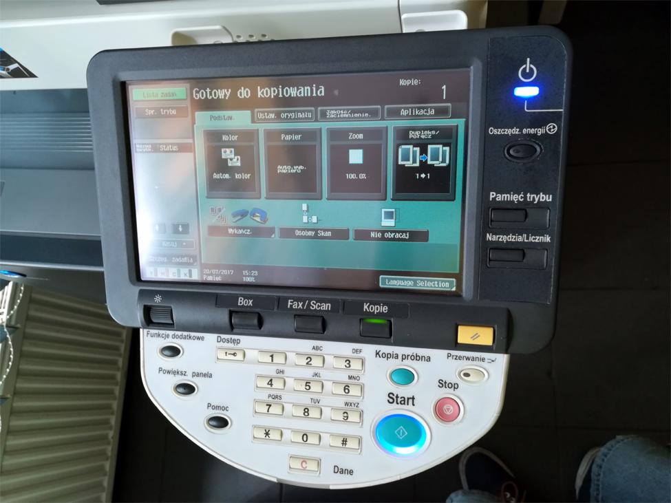 Panel sterowania kserokopiarki A3 z podświetlonym przyciskiem start i ekranem gotowości do kopiowania, widoczne ustawienia kolorów, papieru i zoomu.