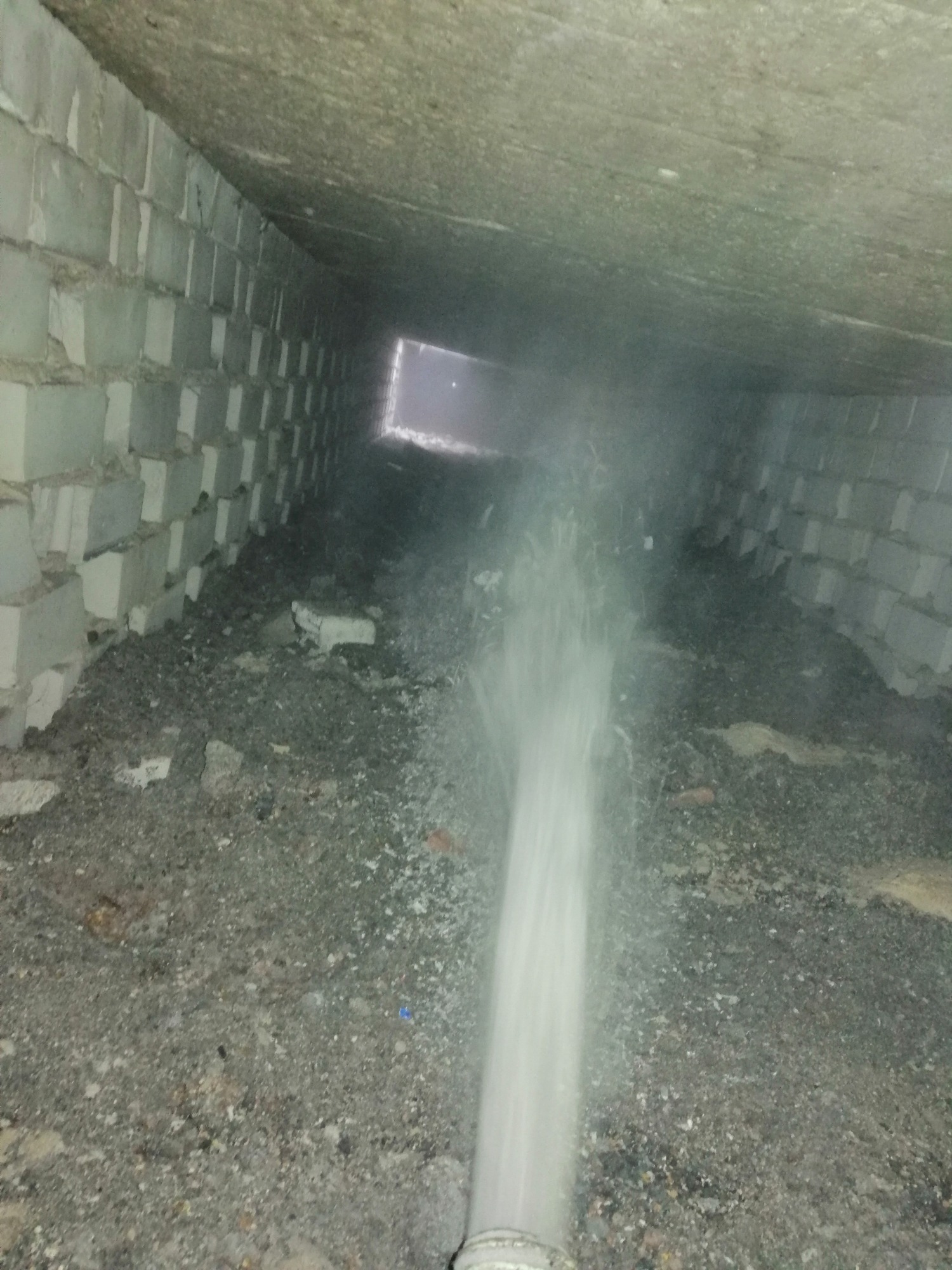 Strumień wody pod ciśnieniem skierowany na gruzowisko wewnątrz murowanego poddasza z widocznym otworem w tle.