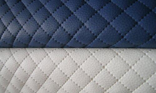 Bliskie ujęcie pikowanej tkaniny w kolorze granatowym i białym z widocznymi przeszyciami tworzącymi wzór rombów.