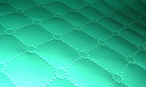 Turkusowa, pikowana tkanina ultradźwiękowo z wzorem rombów połączonych okręgami z małych kropek, widoczna pod kątem.