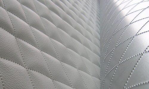 Szczegółowe ujęcie ultradźwiękowo pikowanej, białej tkaniny w romby, wykonanej w Łodzi, z widocznymi przeszyciami i fakturą materiału.