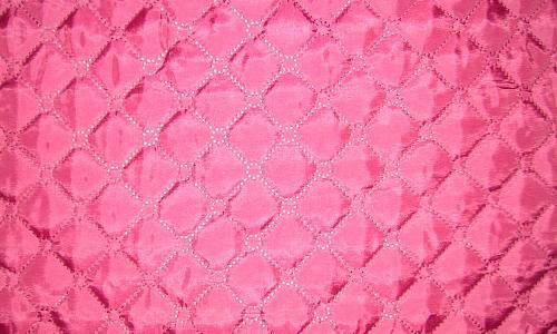 Różowa tkanina pikowana w romby, z delikatnym połyskiem i widoczną fakturą szwów.