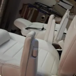 Białe, skórzane fotele samochodowe z regulowanymi zagłówkami i podłokietnikami, widoczne w warsztacie.