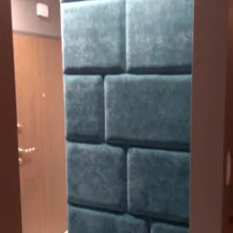 Turkusowy panel tapicerowany z siedziskiem w przedpokoju, widoczny fragment drzwi wejściowych.