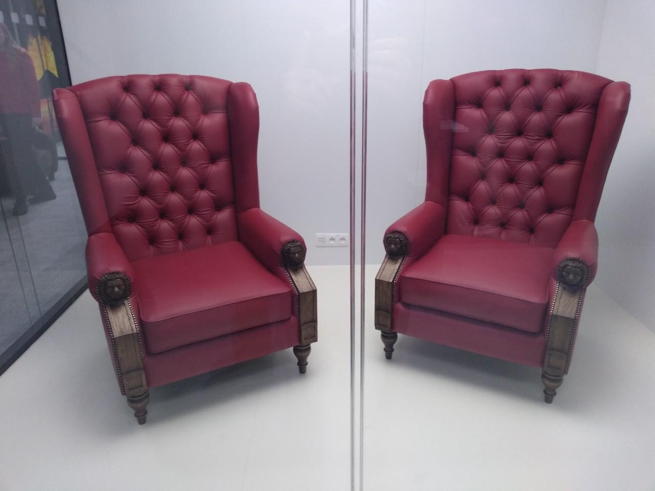 Dwa identyczne, bordowe fotele typu uszak z pikowanym oparciem i drewnianymi elementami zdobionymi rzeźbami, ustawione obok siebie na białym tle.