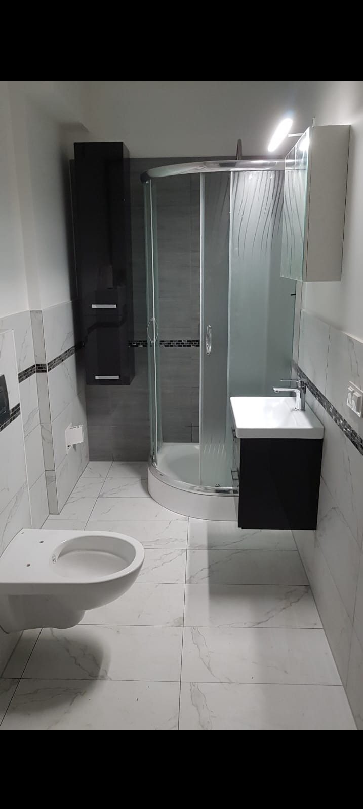 Nowoczesna aranżacja łazienki w Szczecinie: kabina prysznicowa z wzorem, białe płytki imitujące marmur, czarne szafki wiszące i umywalka. Eleganckie wykończenie.