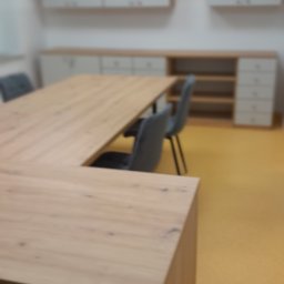 F.H.P.U.DREWMAK - Jasny, drewniany blat biurka w kształcie litery U z szarymi krzesłami, na tle białych szafek z drewnianymi akcentami i żółtej podłogi. Ujęcie z bliska, lekko rozmyte.