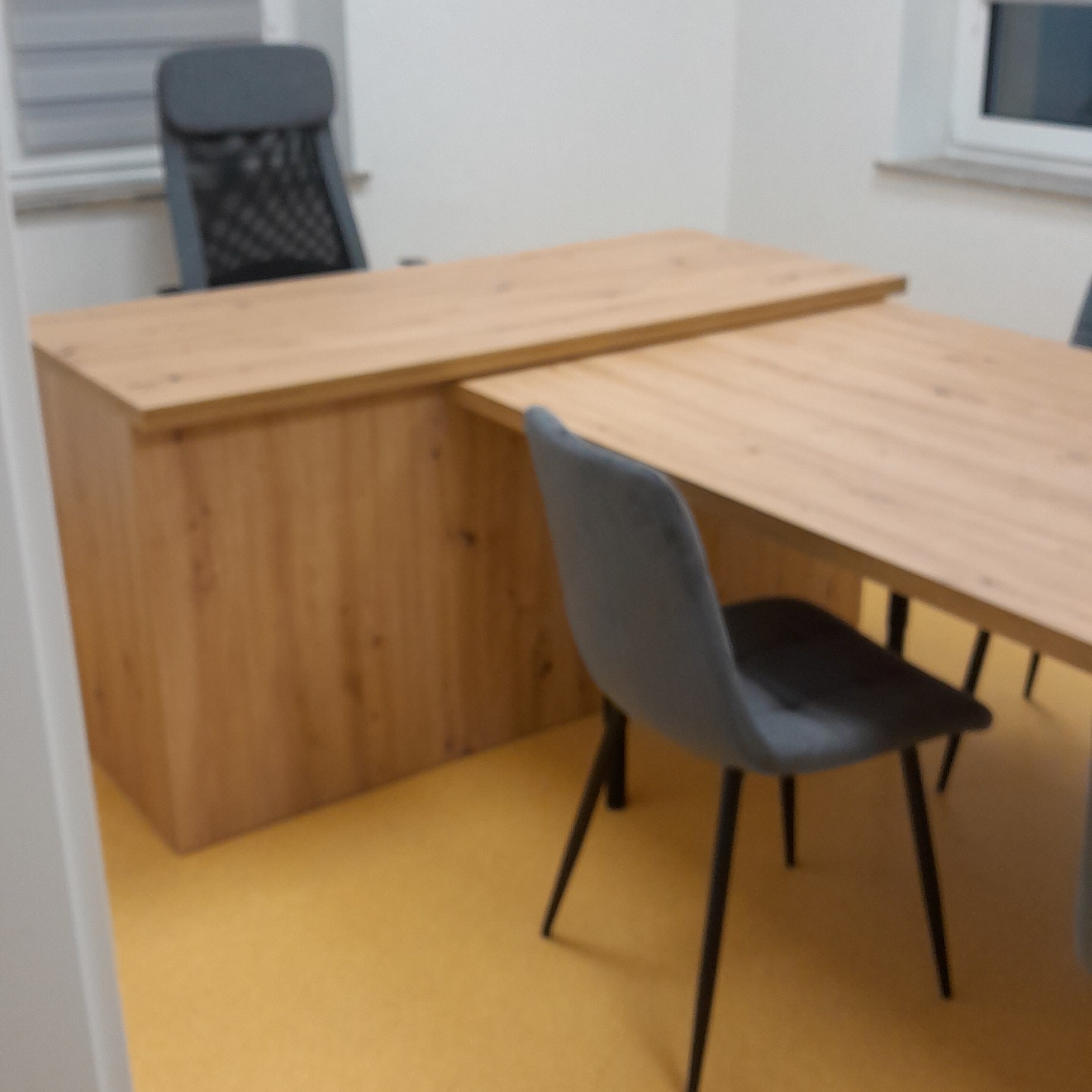 Drewniany blat biurka na wymiar z szarą tapicerowaną krzesłem w nowoczesnym biurze. Jasne wnętrze, minimalistyczny design.