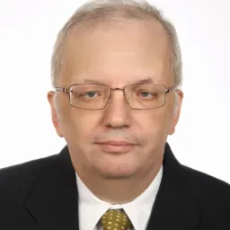 Portret mężczyzny w okularach, marynarce i krawacie z drobnym wzorem, na białym tle.