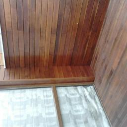 Korsuper - Drewniana elewacja budynku w Warszawie, widziana z dołu, z fragmentem okna z zasłoną w tle.