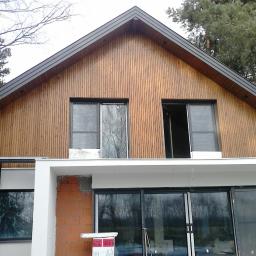 Korsuper - Dom w trakcie ocieplania, z widoczną drewnianą elewacją, niezakończonym ociepleniem ściany z cegły oraz rusztowaniem po lewej stronie.