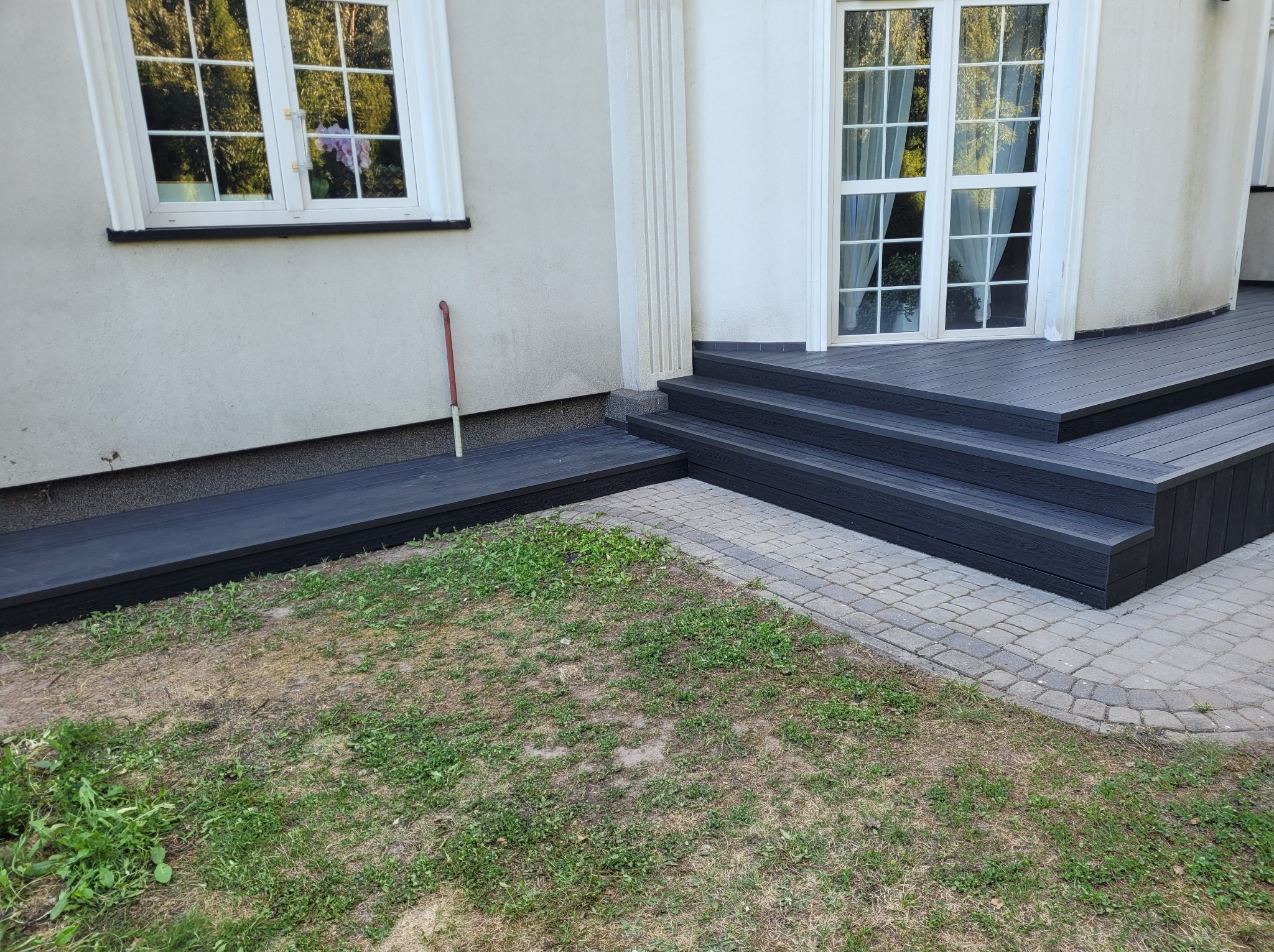 Ciemnoszara, kompozytowa platforma z trzema stopniami prowadząca do białych drzwi balkonowych, z widoczną kolumną dekoracyjną i fragmentem trawnika.