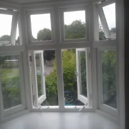 Wielokwaterowe, białe okno w wykuszu z częściowo otwartymi skrzydłami, widok na zieleń ogrodu i plac zabaw.