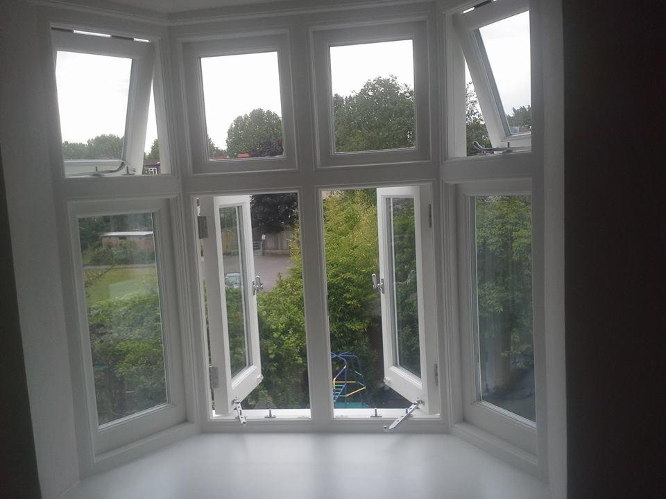 Wielokwaterowe, białe okno w wykuszu z częściowo otwartymi skrzydłami, widok na zieleń ogrodu i plac zabaw.