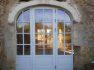 Białe, łukowe drzwi wejściowe z licznymi szybkami, osadzone w kamiennej fasadzie budynku.