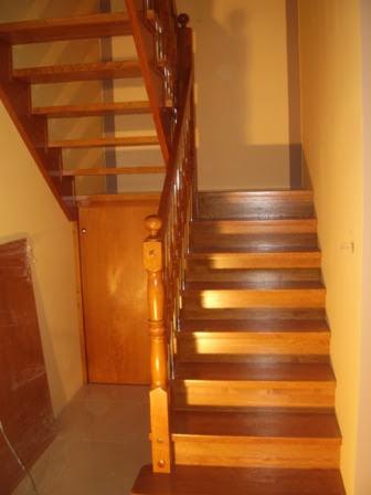 Klatka schodowa z drewnianymi schodami i balustradą z toczonymi elementami, widok z dołu na pierwsze stopnie, drzwi w tle.