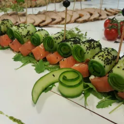 Elegancko podane roladki z łososia i og&oacute;rka z czarnuszką na rukoli, uzupełnione pomidorkami koktajlowymi i plastrami pieczonego mięsa, tworzące wykwintną kompozycję.