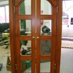 Dębowe dwuskrzydłowe drzwi wewnętrzne z szybami, widoczne narzędzia stolarskie w tle.