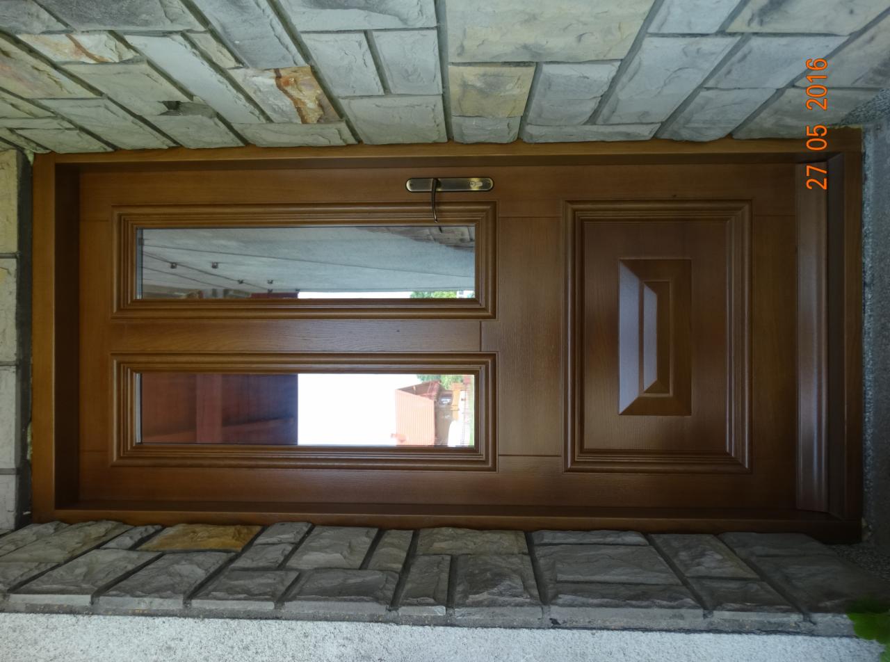 Brązowe drzwi wejściowe z dwoma poziomymi przeszkleniami, zamontowane w kamiennym portalu, widoczne z bliska, z datą 27.05.2016 w prawym górnym rogu.