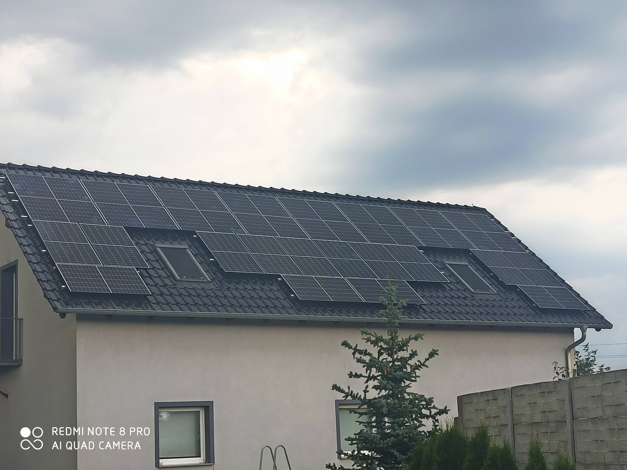 Instalacja paneli słonecznych na dachu domu jednorodzinnego z oknami dachowymi, widok na pochmurne niebo.