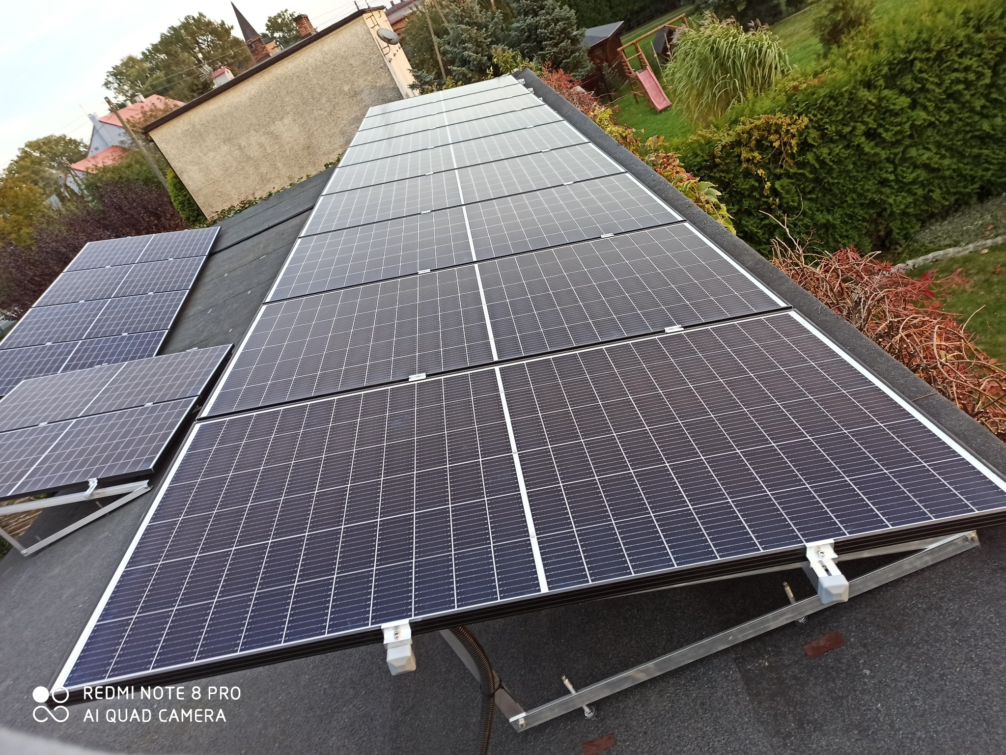 Instalacja fotowoltaiczna na dachu domu jednorodzinnego, widok z góry, w tle ogród z elementami placu zabaw.