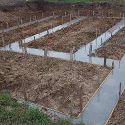 Zalane betonem szalunki fundamentowe w ziemi, widoczne drewniane podpory i wykop pod budowę domu.