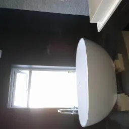 Nowoczesna łazienka z wolnostojącą białą wanną, toaletą i oknem z jasnym światłem dziennym, ściany w ciemnym kolorze, widok z góry.