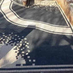 Czarno-beżowa kostka brukowa ułożona we wzór z motywem pikseli i falującej wstęgi, widok z góry na ukończoną nawierzchnię.