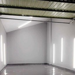 DM Design Damian Mielczarek - Wnętrze pomieszczenia po szpachlowaniu ścian i położeniu ciemnej, błyszczącej podłogi, widoczne pionowe lampy na ścianach.