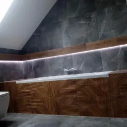 Nowoczesna łazienka na poddaszu: szare płytki imitujące marmur na ścianach, drewnopodobne panele z geometrycznym wzorem przy wannie, podświetlenie LED, szara podłoga i fragment toalety.