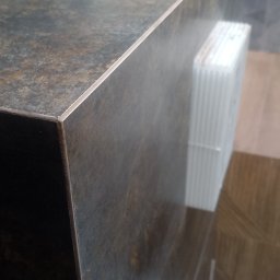 DM Design Damian Mielczarek - Wykończona powierzchnia blatu z płytek imitujących kamień, widoczne narzędzia i materiały budowlane na blacie oraz w tle, sugerujące prace wykończeniowe w toku.