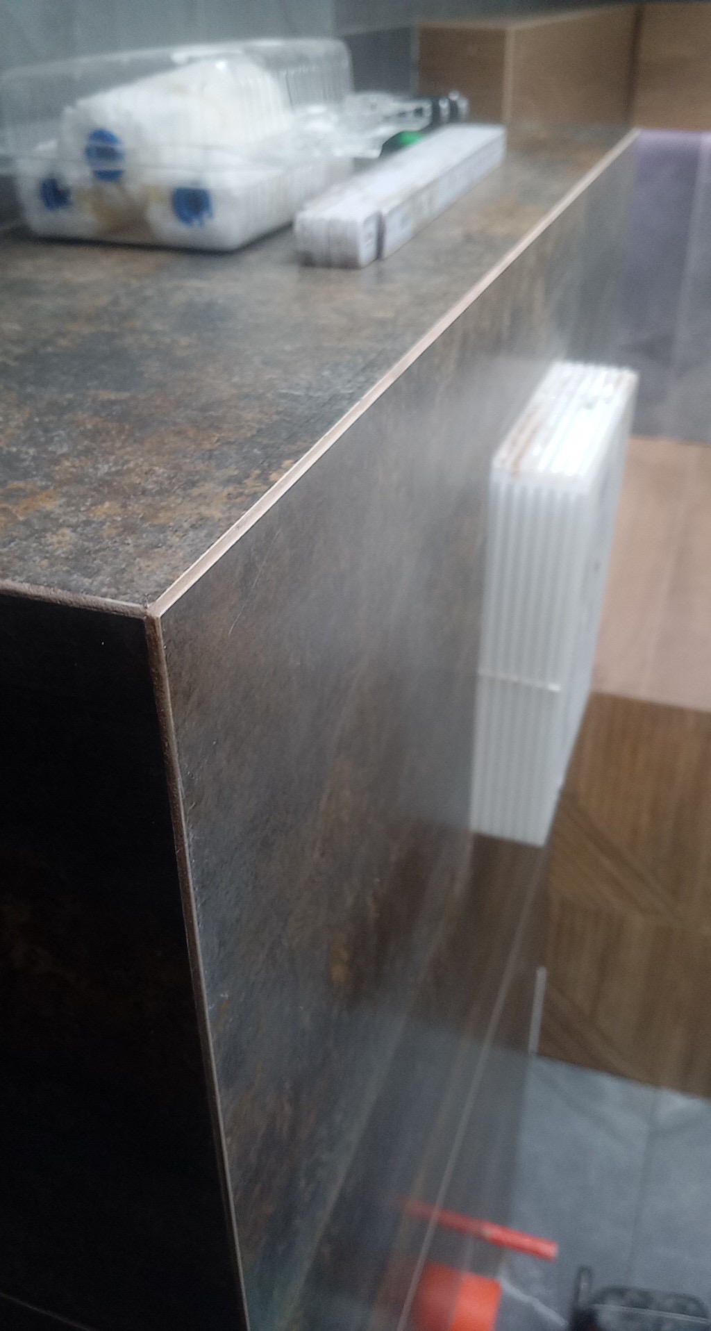 Wykończona powierzchnia blatu z płytek imitujących kamień, widoczne narzędzia i materiały budowlane na blacie oraz w tle, sugerujące prace wykończeniowe w toku.