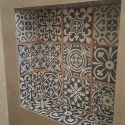 Wnęka w ścianie wykończona dekoracyjnymi, niebiesko-białymi płytkami ceramicznymi o zróżnicowanych wzorach, fugi w kolorze naturalnego drewna.