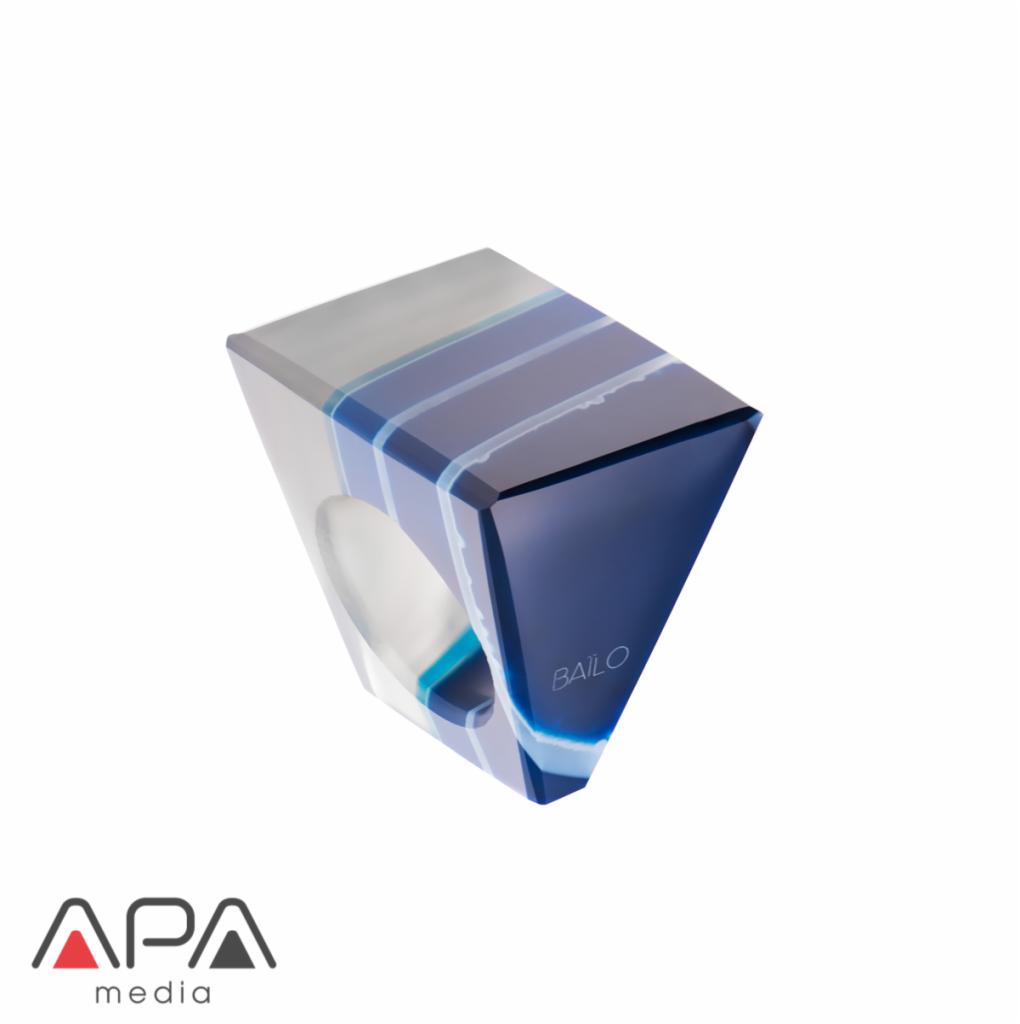 Kwadratowy pierścionek z żywicy epoksydowej w odcieniach błękitu i szarości, z widocznym logo 'BAILO', sfotografowany na białym tle w studio.