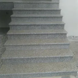 Zewnętrzne schody z szarego kamienia o drobnej fakturze, prowadzące do drzwi wejściowych, otoczone drobnym żwirem.