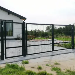 Nowoczesna posesja z czarną bramą panelową otwieraną dwuskrzydłowo i furtką, skrzynka pocztowa przy wejściu do domu.