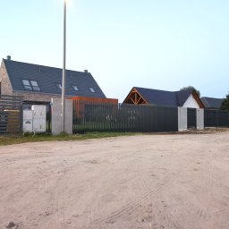 LIVBET-ECO - Ogrodzenia Systemowe - Nowoczesne, poziome ogrodzenie panelowe w kolorze grafitowym, z betonowymi słupkami, na tle nowo wybudowanych domów jednorodzinnych i piaszczystej drogi.