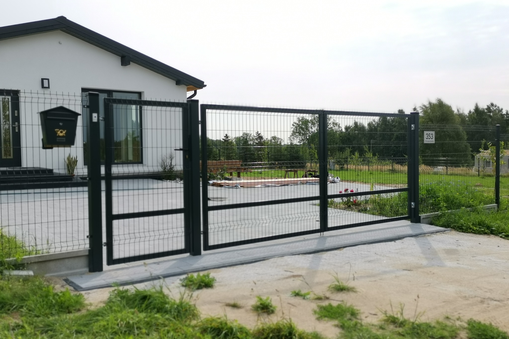 Nowoczesna posesja z czarną bramą panelową otwieraną dwuskrzydłowo i furtką, skrzynka pocztowa przy wejściu do domu.