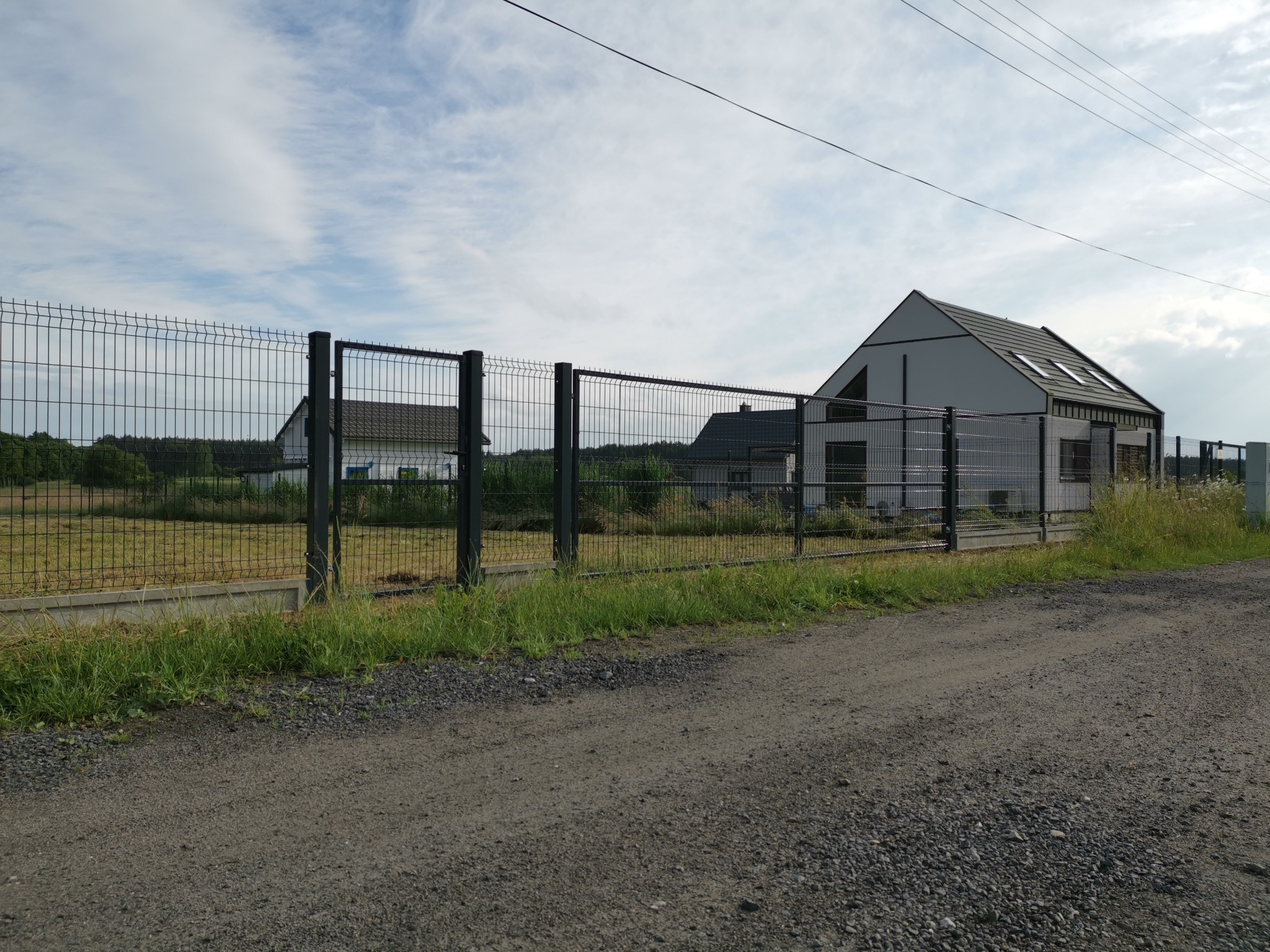 Szare ogrodzenie panelowe z furtką, zabezpieczające posesję z nowoczesnym domem w tle, Kamień Pomorski.